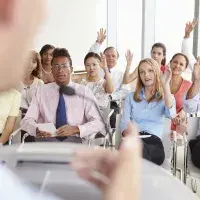 Ein Vortragender und eine zuhörende Gruppe, einige zeigen auf